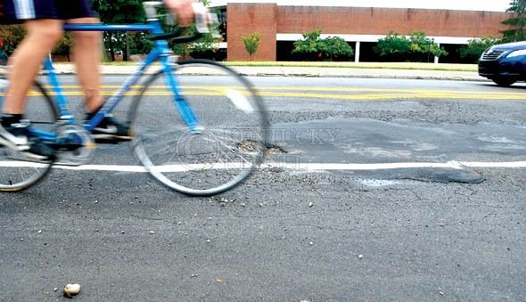 Everett Cislo//Kentucky Kernel
 A cyclist bikes past the potholes on August 24 on Avenue of Champtions. Both bikers and drivers must be wary of the large potholes on Avenue of Champsions.