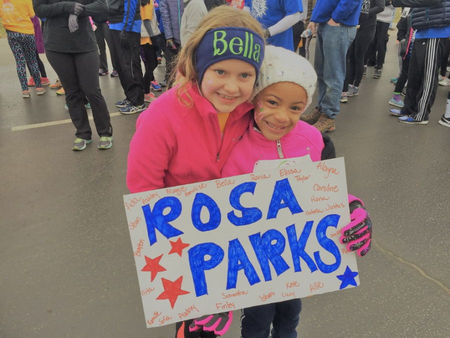 Two Girls on the Run participants hold up a sign displaying a female role model at a previous GOTR 5k race.