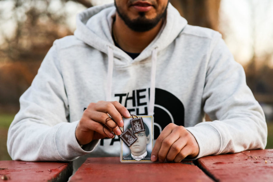 Omar, a Lexington resident protected by DACA, poses with a photo of Santo Toribio Romo, the saint of the immigrants, and a necklace with photos of saints on Wednesday, December 4, 2019, in Lexington, Kentucky. “The necklace with the saints represents protection to me,” Omar said. Omar said the necklace was a gift from his mom when he was young, and he still keeps it in his wallet. Omar said he has heard stories about Santo Toribio Romo, the saint in the larger photo, for a long time. “It’s said that when an immigrant is wanting safe passage on their journey, they pray to him for protection.” Photo by Michael Clubb | Staff