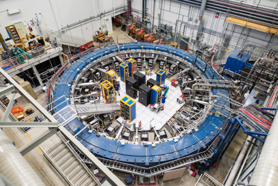 The Muon g-2 ring sits in its detector hall amidst electronics racks and the muon beamline. This experiment studies the precession (or wobble) of muons as they travel through the magnetic field. 