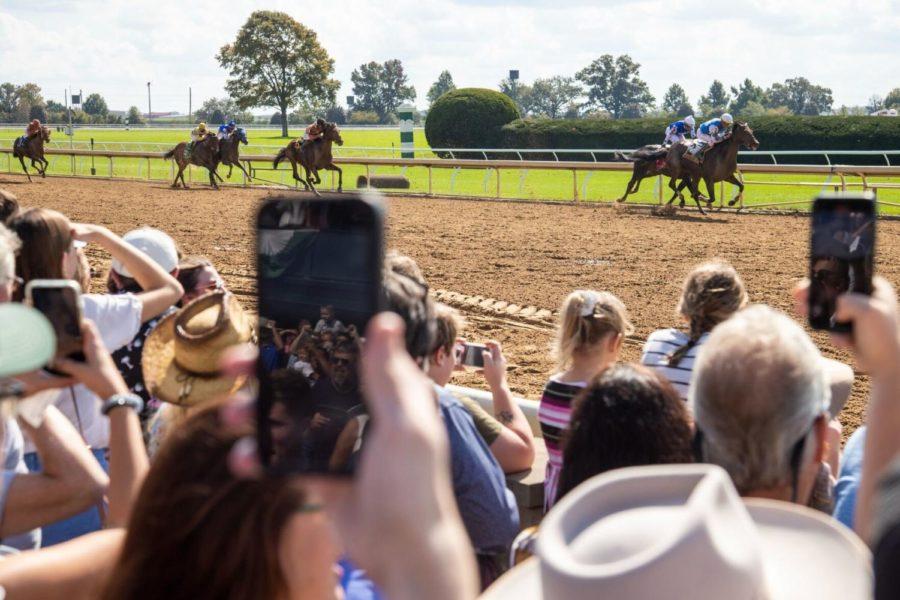 Patrons hold up phones and watch as horses cross the finish line in an undercard race during the opening day of Keenelands Fall Meet in Lexington, Kentucky, on Oct. 8, 2021.