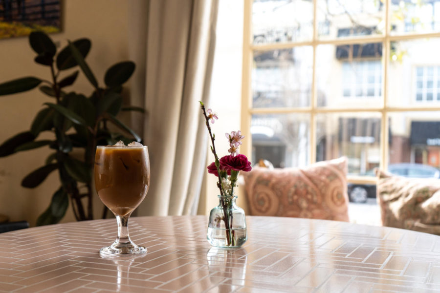 A cup of dirty chai tea latte sits on a table next to a small flower arrangement on Tuesday, April 4, 2023, at Brevede Coffee Chevy Chase in Lexington, Kentucky. Photo by Carter Skaggs | Staff