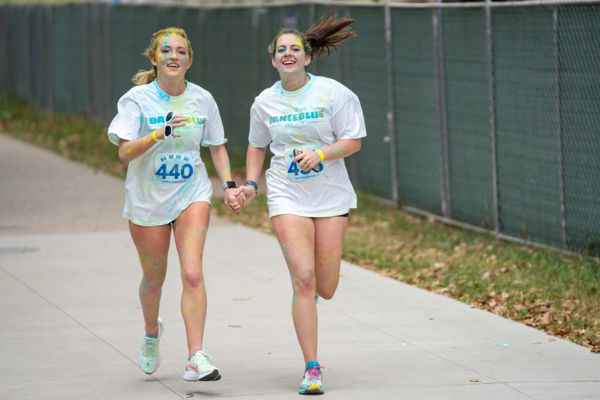 Two runners hold hands while running during the Dance Blue 5K Color Run on Sunday, Oct. 8, 2023, at the University of Kentucky in Lexington, Kentucky. Photo by Travis Fannon | Staff