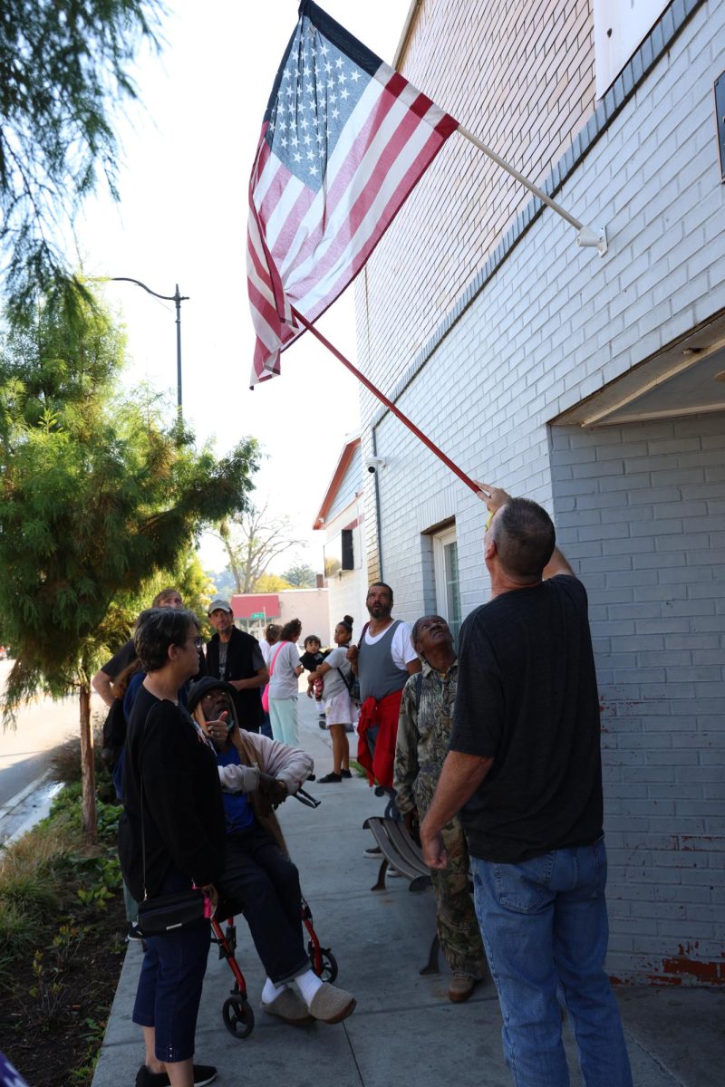 People wait outside the doors of the ACCESS Soup Kitchen and Men’s Shelter while Brian Pedigo fixes the flag of the United States on Thursday, Oct. 12, 2023 in Frankfort, Ky. Photo by Hannah Stanley