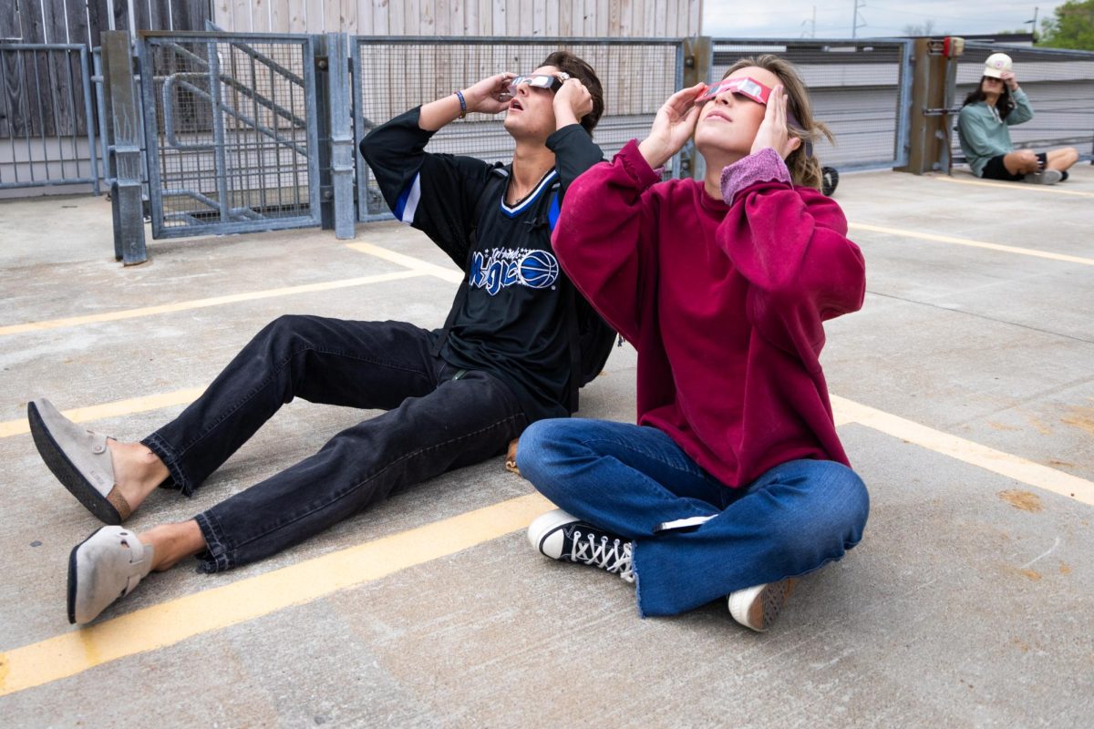 Students Gabriel Rios, left, and Caroline Coleman view the partial solar eclipse on Monday, April 8, 2024, on top of the Center Court Parking Garage in Lexington, Kentucky. Photo by Samuel Colmar | Staff