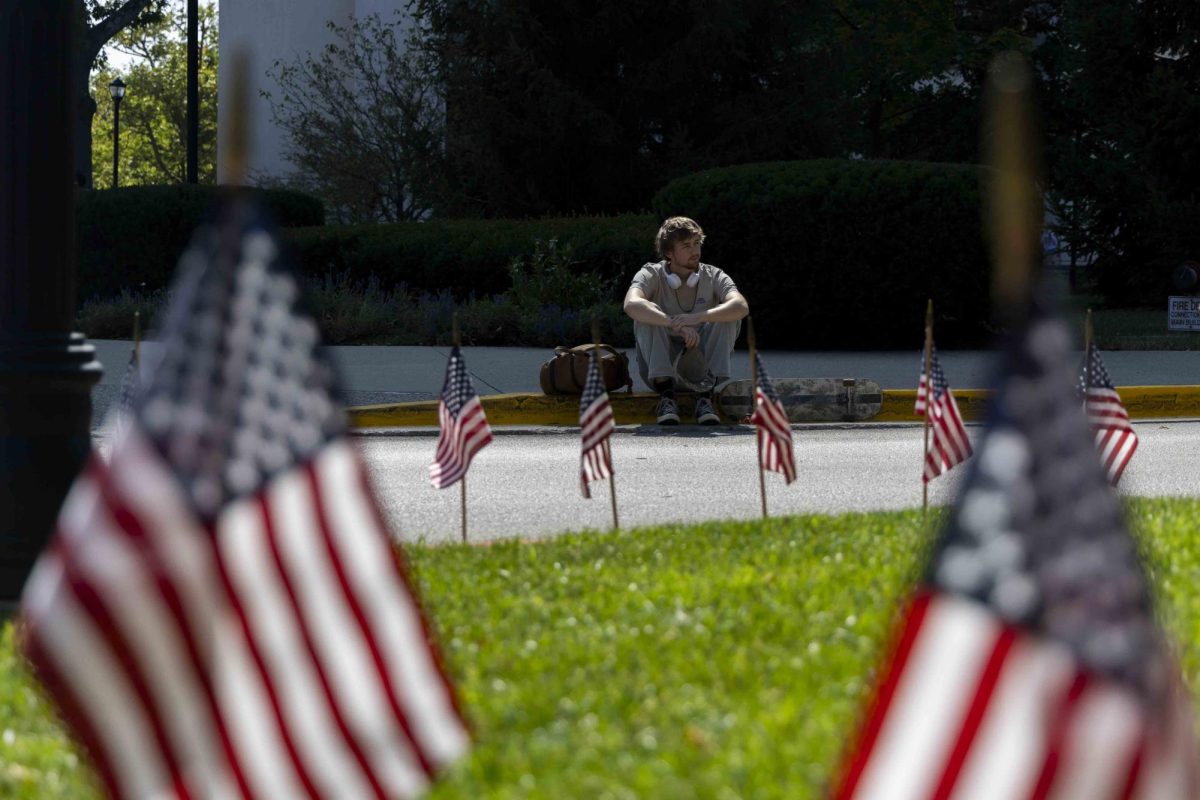 Thomas Ruberg, a junior Psychology major, sits on the curb and listens to the 9/11 memorial presentation on Wednesday, Sept. 11, 2024, at The Main Building in Lexington, Kentucky. Photo by Matthew Mueller | Staff