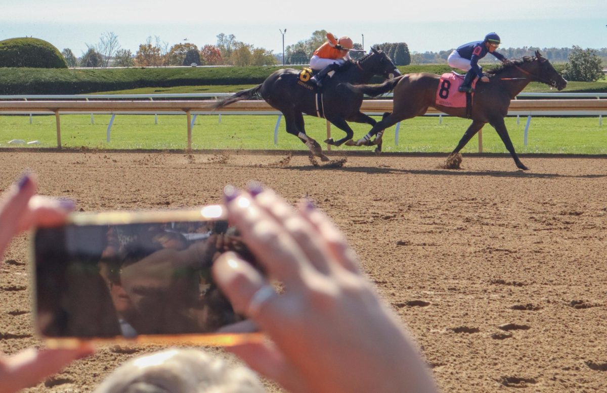 A student takes a video as horses pass the finish line during Keeneland College Scholarship Day on Friday, Oct. 18, 2024, at Keeneland in Lexington, Kentucky. Photo by Mateo Smith Villafranco | Staff