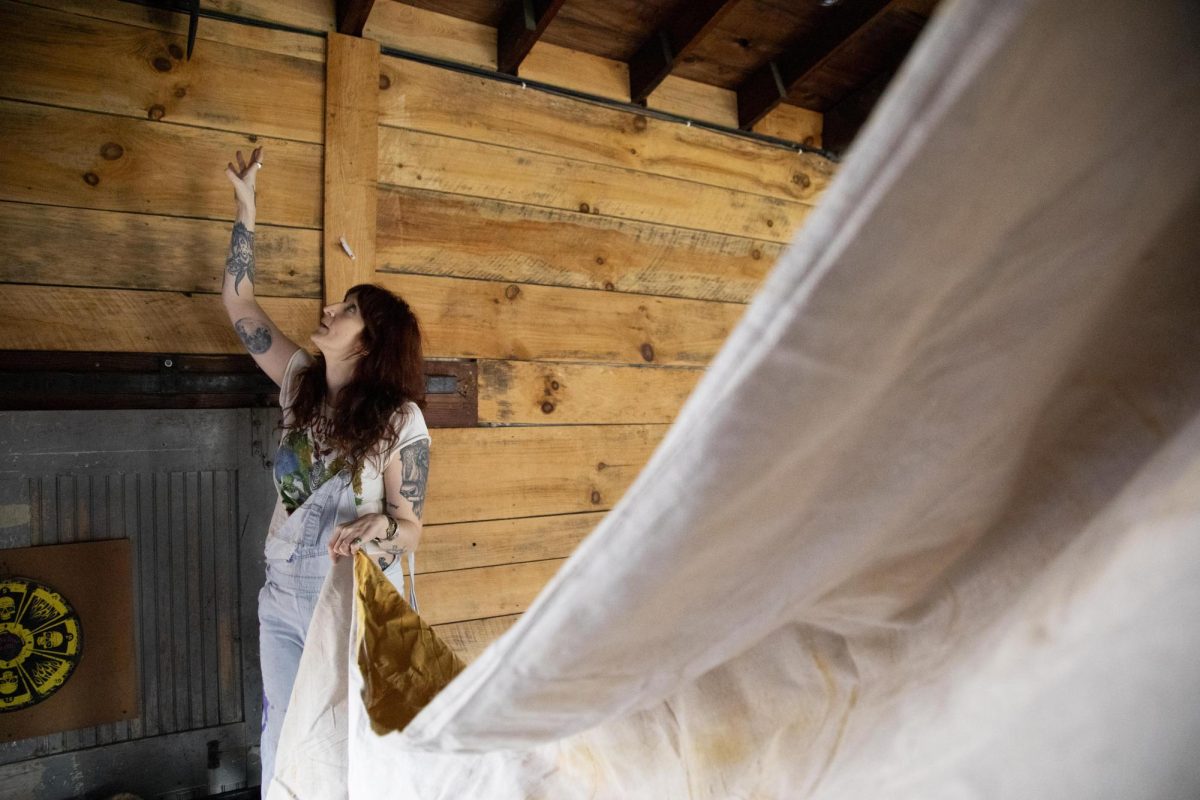 Anna Pollock hangs a tarp to the rafter of the stage on Friday, Dec. 13, 2024, at The Burl in Lexington, Kentucky. Photo by Christian Kantosky | Assistant Photo Editor