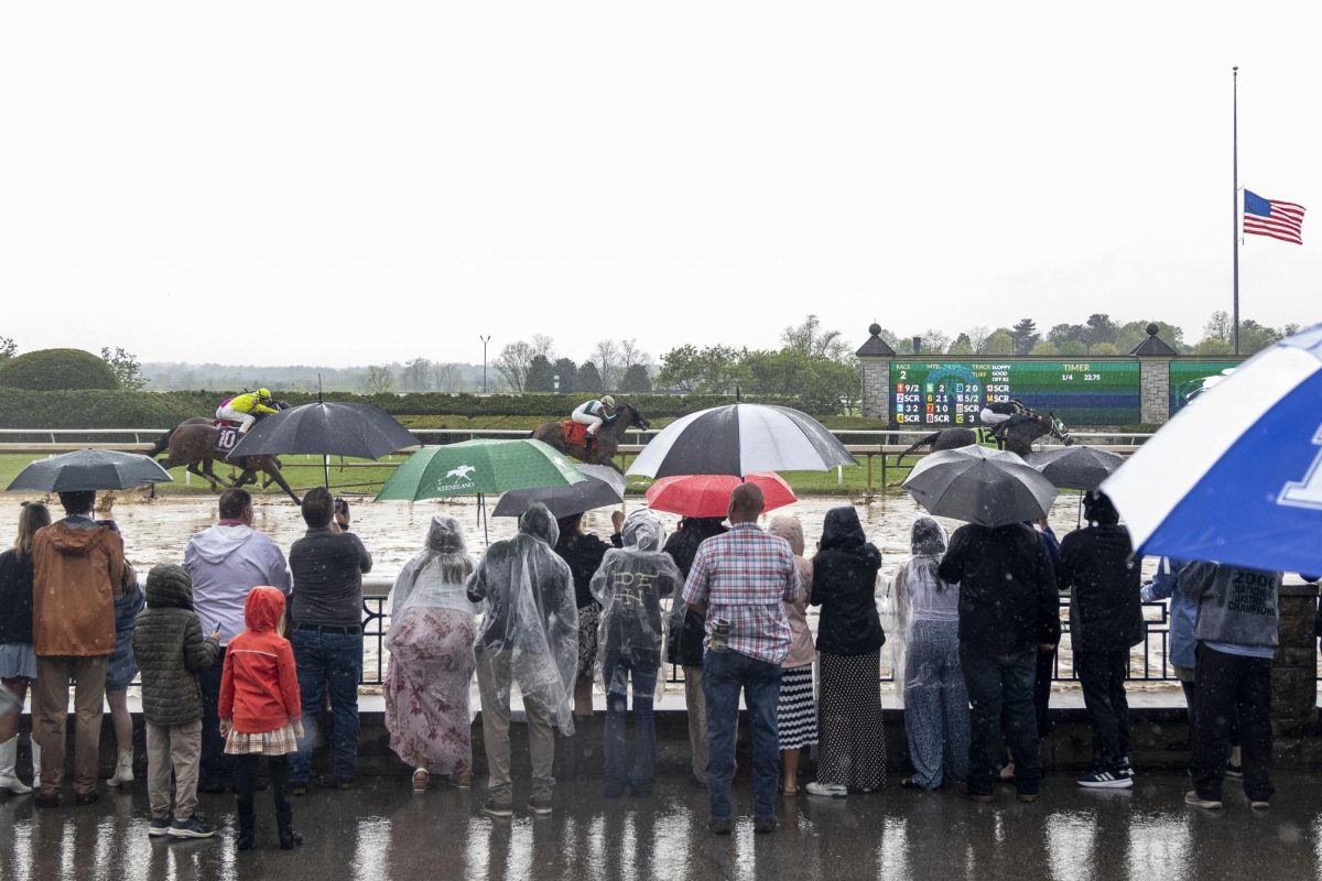 Horses race by while spectators watch beneath umbrellas during Spring Closing Day on Friday, April 25, 2025, at Keeneland Racetrack in Lexington, Kentucky. Photo by Sydney Novack | Staff